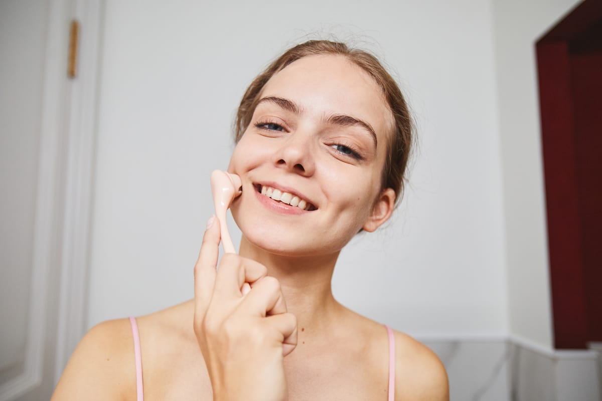 Femme pratiquant un auto-massage facial avec un gua sha sur joue et cou